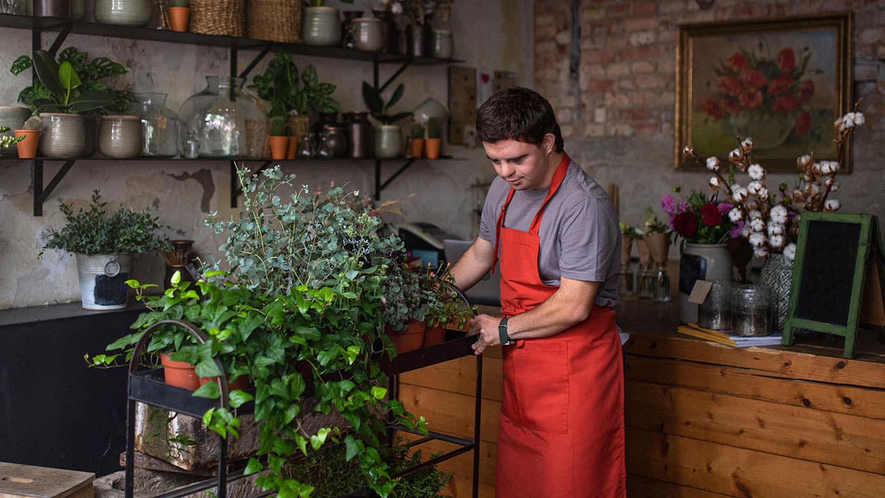 Young male florist with Down syndrome taking care of plants in flower shop