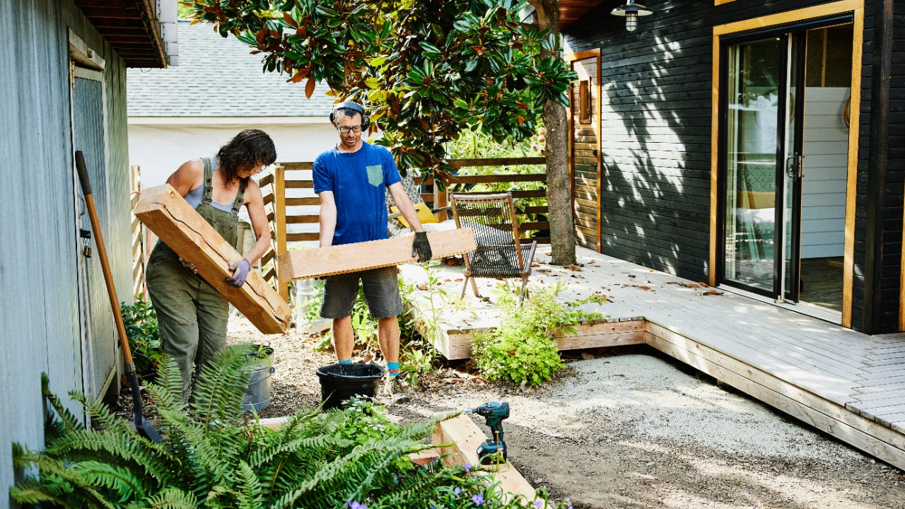 A couple carries lumber to build garden beds in the backyard.